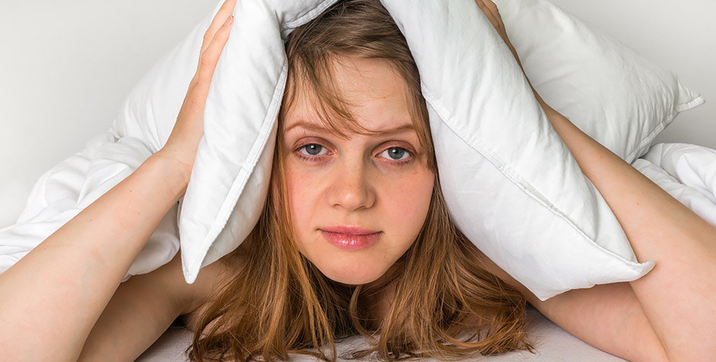 tired looking female in bed holding pillow over her ears